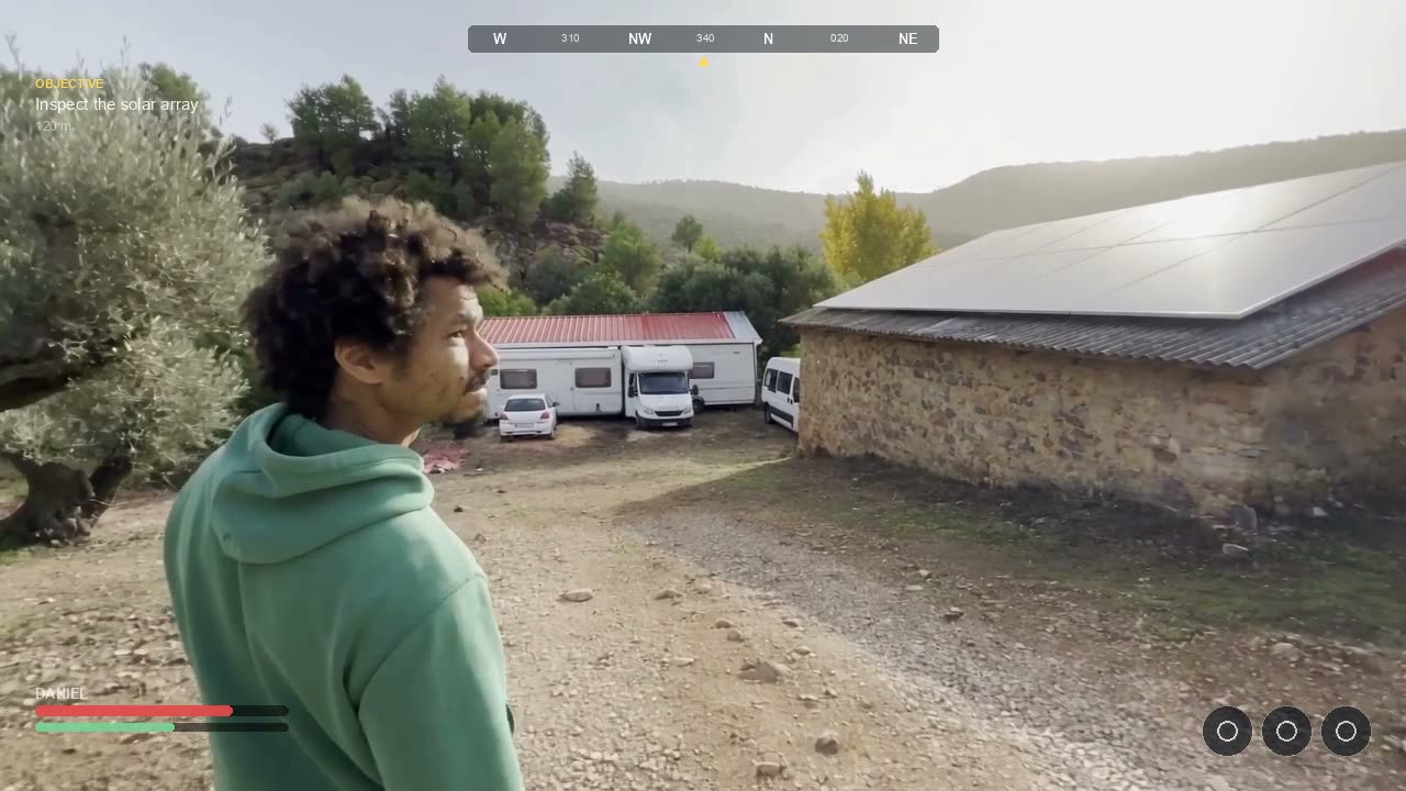 Concept render: over the shoulder of Daniel in a green hoodie, looking toward the caravans, the red-roofed building and a stone house with solar panels